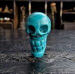 Hand-carved turquoise skull amulet with a natural dark matrix.