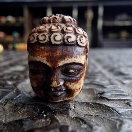 Hand-carved Buddha head amulet featuring a serene expression and weathered ritual patina.
