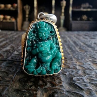 A small, intricately hand-carved Buddha figure made from natural blue-green Tibetan turquoise.