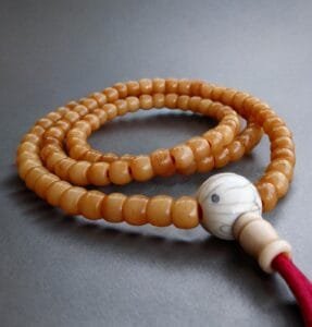 A strand of 108 antique yak bone beads showing a rich, aged yellow patina and smooth surface.