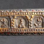 Horizontal view of a 19th-century Tibetan wood scripture cover showing three detailed hand-carved Buddha figures.