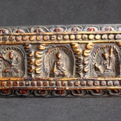 Horizontal view of a 19th-century Tibetan wood scripture cover showing three detailed hand-carved Buddha figures.