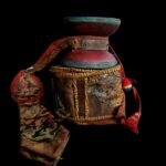 A vintage hourglass-shaped Tibetan damaru drum featuring aged wood and stretched leather skins with traditional beaters