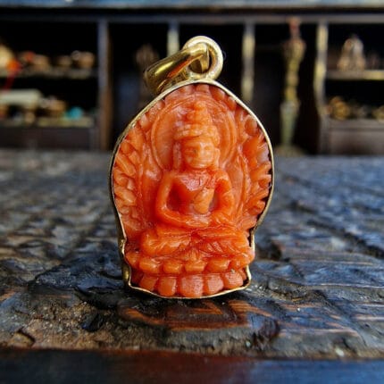 Tibetan coral Buddha Shakyamuni amulet hand-carved red-orange stone in gold-toned metal casing.