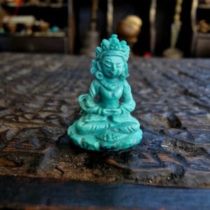 Himalayan turquoise Buddha amulet hand-carved crowned seated figure in meditation pose on dark wooden surface.
